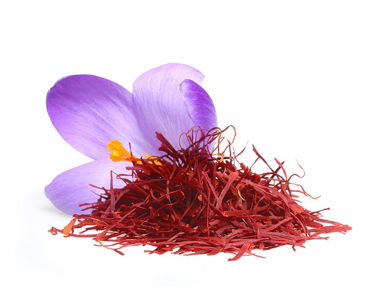 Eine lila Krokusblüte liegt neben einem Haufen von roten Safranfäden. Der Kontrast zwischen der Blüte und den Fäden hebt die Farbe und Textur hervor.