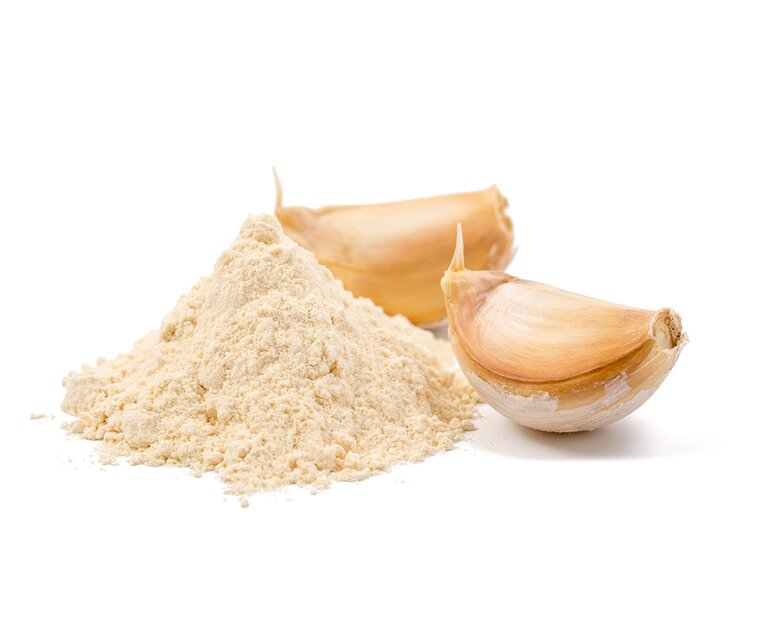 Ein Haufen Knoblauchpulver mit zwei frischen Knoblauchzehen daneben.