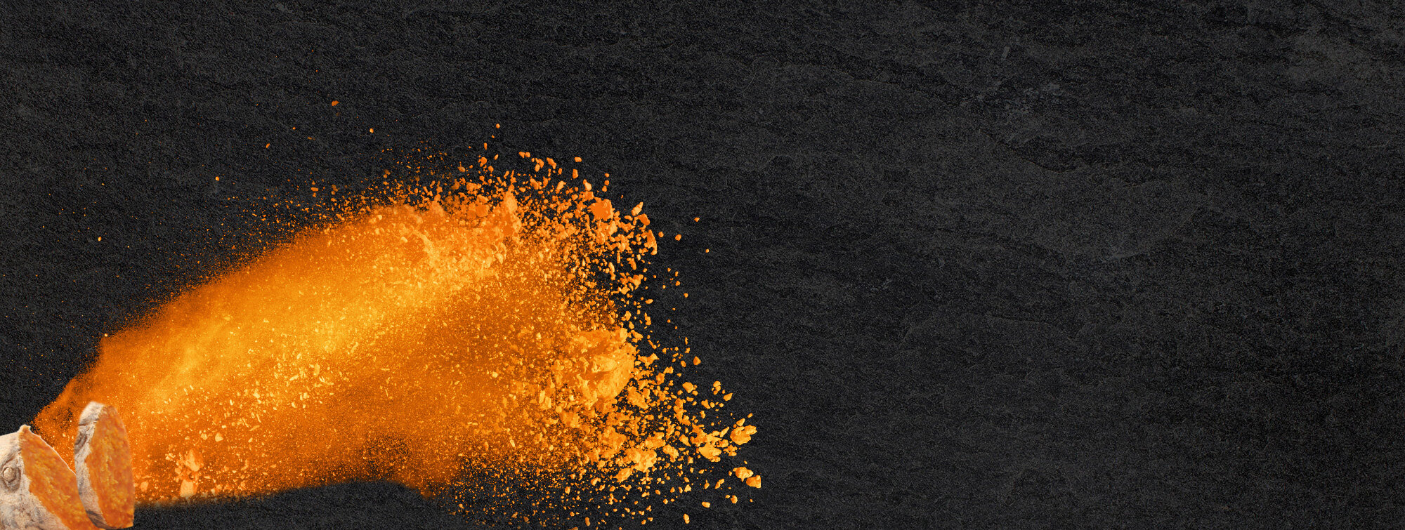 Ein orangefarbener Staub oder Pulver wird von einer linken Ecke auf einem schwarzen Hintergrund in die Mitte aufgewirbelt. Der Staub wirkt dynamisch und strahlt Energie aus.